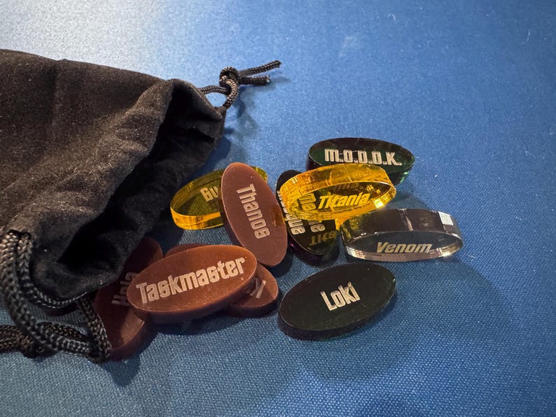 Marvel Villainous random tokens spilling out of the black velvet bag they come in. This set currently includes 12 villain tokens so you can randomize who everyone plays.