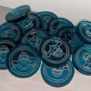Pu&ograve; includere: Un mucchio di gettoni da gioco blu turchese con un design inciso bianco di una creatura alata.