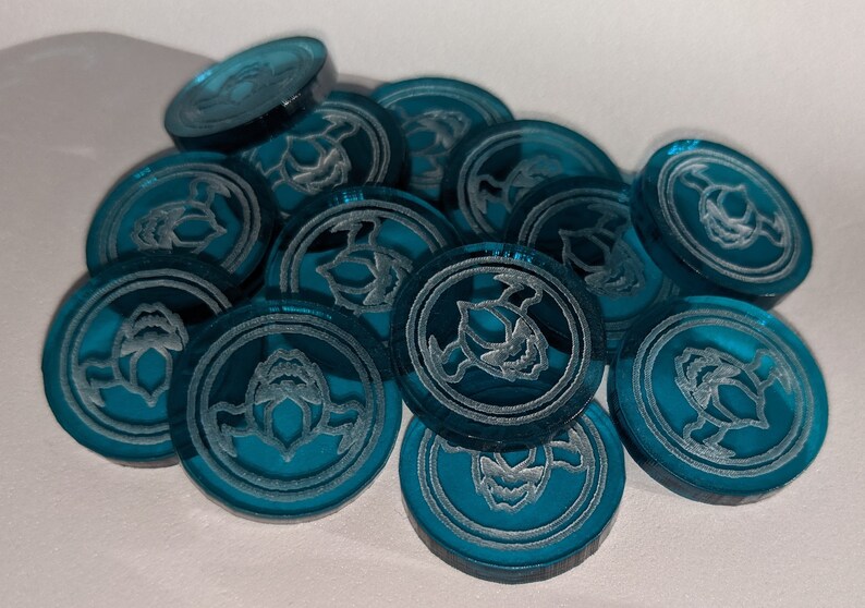 Pu&ograve; includere: Un mucchio di gettoni da gioco blu turchese con un design inciso bianco di una creatura alata.