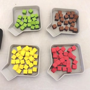 May include: Four white trays with a small spout on the side, each filled with a different color of small square blocks. The trays contain green, brown, yellow, and red blocks.