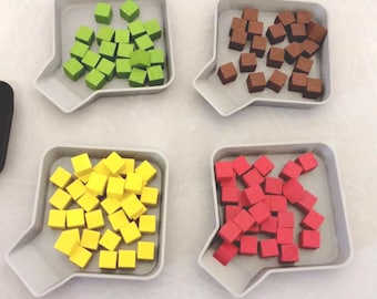 May include: Four white trays with a small spout on the side, each filled with a different colour of small square blocks. The trays contain green, brown, yellow, and red blocks.