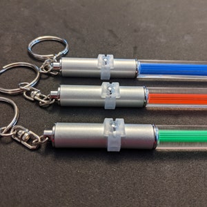 Peut inclure: Trois lampes de porte-cl&eacute;s argent&eacute;es avec des tubes en plastique transparent. Les tubes sont remplis de filaments de couleur bleue, orange et verte. Chaque lampe a un anneau argent&eacute; avec un bouton en plastique transparent.