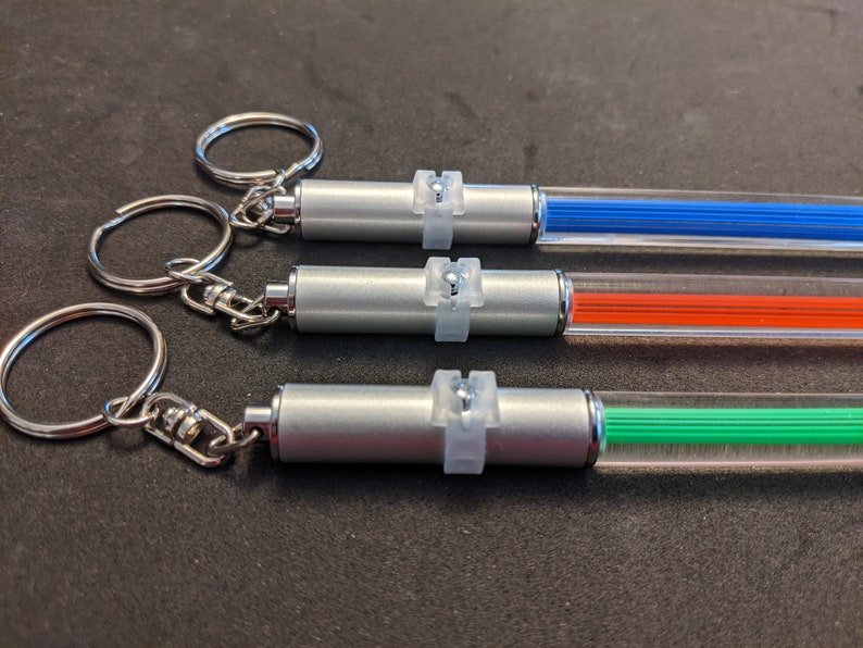 Peut inclure: Trois lampes de porte-cl&eacute;s argent&eacute;es avec des tubes en plastique transparent. Les tubes sont remplis de filaments de couleur bleue, orange et verte. Chaque lampe a un anneau argent&eacute; avec un bouton en plastique transparent.