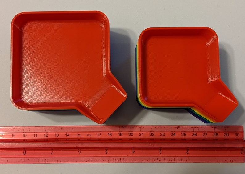 Top view of the two different sized stackable game trays shown alongside a red ruler so they can be measured.