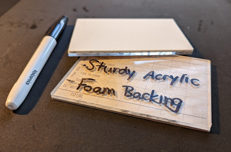 May include: A clear acrylic sheet with a grid pattern and the words "Sturdy Acrylic Foam Backing" written in black marker.