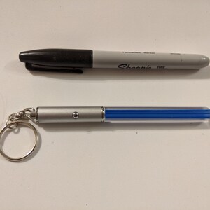 Peut inclure: Un porte-cl&eacute;s argent&eacute; avec un stylo lumineux bleu attach&eacute;. Le stylo a un petit bouton sur le c&ocirc;t&eacute;. Le porte-cl&eacute;s est attach&eacute; &agrave; un anneau argent&eacute;.