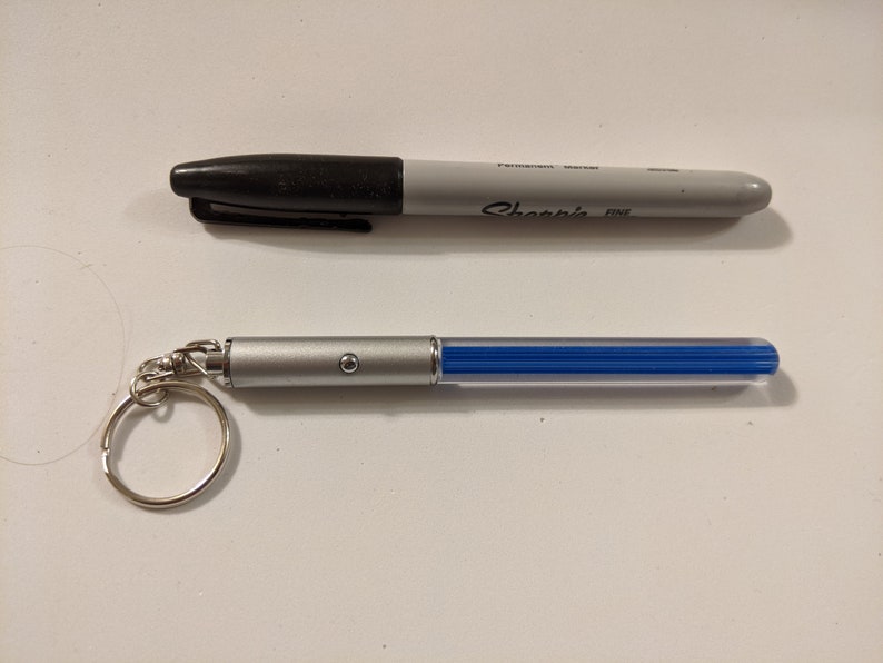 Peut inclure: Un porte-cl&eacute;s argent&eacute; avec un stylo lumineux bleu attach&eacute;. Le stylo a un petit bouton sur le c&ocirc;t&eacute;. Le porte-cl&eacute;s est attach&eacute; &agrave; un anneau argent&eacute;.