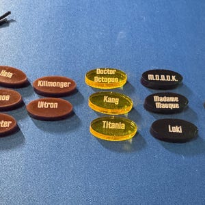 Marvel Villainous random tokens displayed in their four sets with a total of 12 villains tokens shown alongside the black velvet bag that they come in.