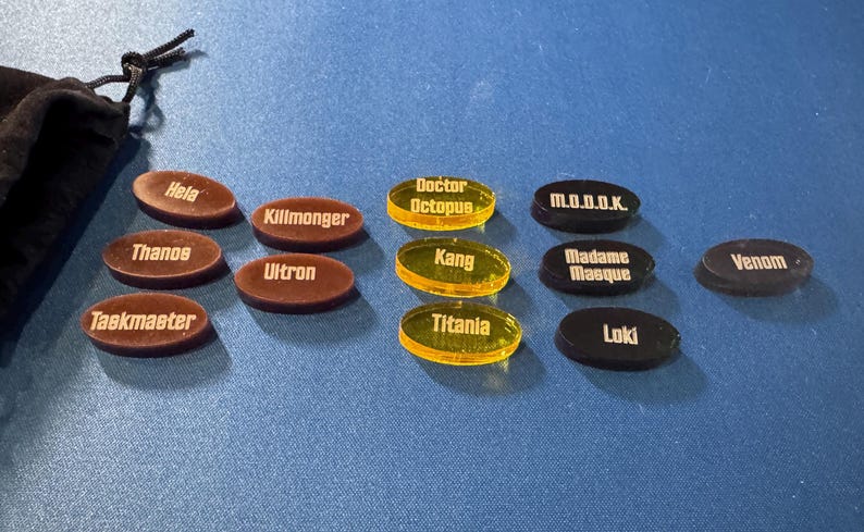 Marvel Villainous random tokens displayed in their four sets with a total of 12 villains tokens shown alongside the black velvet bag that they come in.