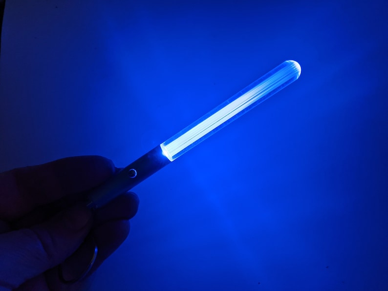 Peut inclure: Un b&acirc;ton lumineux bleu avec une source de lumi&egrave;re blanche. Le b&acirc;ton lumineux est tenu dans une main.