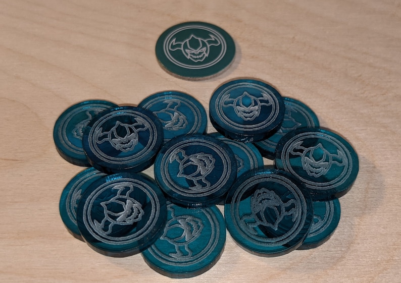 Pu&ograve; includere: Un mucchio di gettoni da gioco blu-verde con un design argentato di una creatura con corna e zanne.