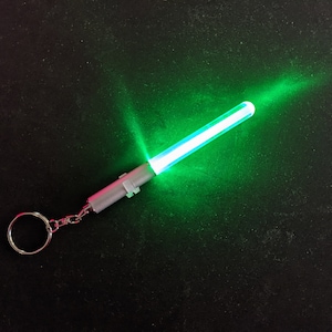 Peut inclure: Un porte-cl&eacute;s argent&eacute; avec un sabre laser lumineux vert attach&eacute;. Le sabre laser est allum&eacute; et &eacute;met une lueur verte brillante.