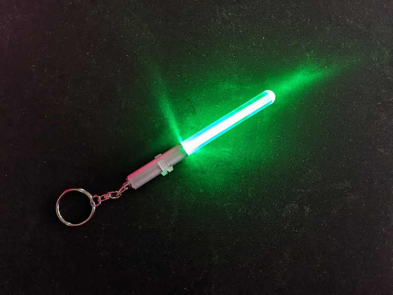 Peut inclure: Un porte-cl&eacute;s argent&eacute; avec un sabre laser lumineux vert attach&eacute;. Le sabre laser est allum&eacute; et &eacute;met une lueur verte brillante.