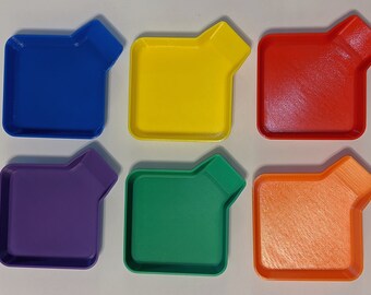 May include: Six brightly coloured, square trays with a distinctive angled corner design. The trays are in blue, yellow, red, purple, green, and orange. The trays are likely plastic and are arranged on a white surface.