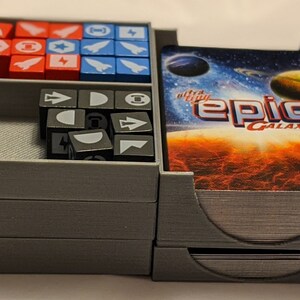 Pu&ograve; includere: Un organizzatore in plastica grigia con tre scomparti per riporre i pezzi di gioco. Lo scomparto superiore contiene un mazzo di carte con il testo "ultra-affy epic galaxies". Lo scomparto centrale contiene dadi grigi con vari simboli. Lo scomparto inferiore contiene cubi rossi, blu e bianchi con simboli.