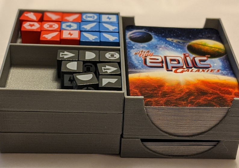 Pu&ograve; includere: Un organizzatore in plastica grigia con tre scomparti per riporre i pezzi di gioco. Lo scomparto superiore contiene un mazzo di carte con il testo "ultra-affy epic galaxies". Lo scomparto centrale contiene dadi grigi con vari simboli. Lo scomparto inferiore contiene cubi rossi, blu e bianchi con simboli.
