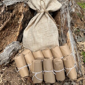 May include: A burlap sack tied with twine sits atop a tree stump, accompanied by several small, brown paper-wrapped packages secured with white string. The scene suggests a rustic, natural theme.