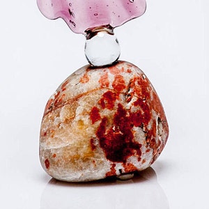 May include: A small, round, red and white stone with a clear glass orb on top. The orb is topped with a pink glass piece.