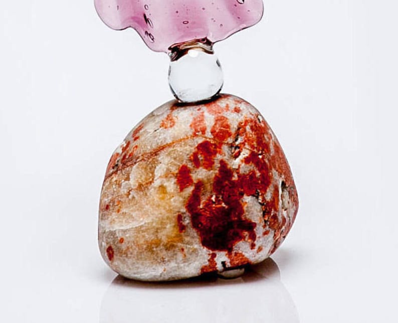 May include: A small, round, red and white stone with a clear glass orb on top. The orb is topped with a pink glass piece.
