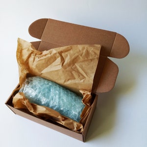May include: A brown cardboard box with the top flap open, revealing a blue glass bottle wrapped in brown paper and bubble wrap.
