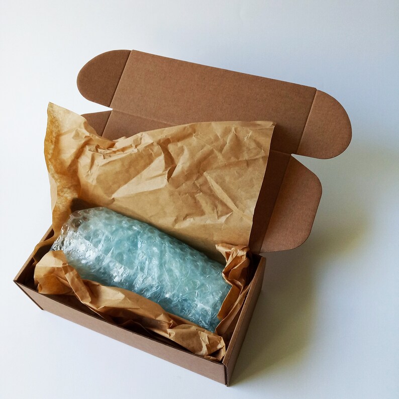 May include: A brown cardboard box with the top flap open, revealing a blue glass bottle wrapped in brown paper and bubble wrap.