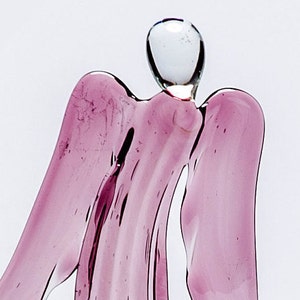 May include: A glass angel figurine with a pink, translucent body and a clear glass head. The angel has wings and a flowing gown.