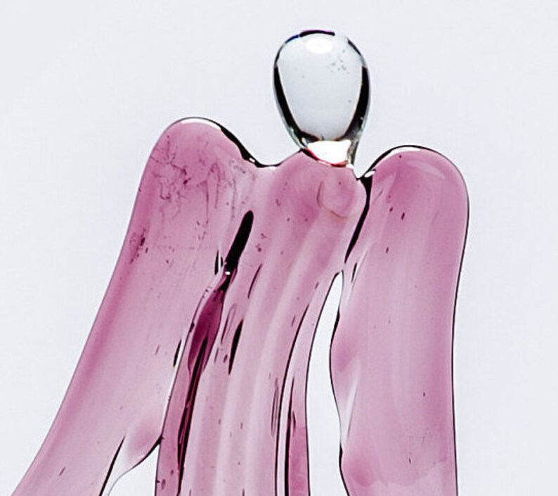 May include: A glass angel figurine with a pink, translucent body and a clear glass head. The angel has wings and a flowing gown.