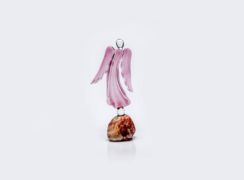 May include: A pink glass angel figurine standing on a brown and white stone base.