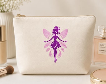 May include: A cream-colored canvas zippered pouch featuring a centered purple graphic of a winged fairy figure. The pouch has a rectangular shape with rounded corners and a gold-toned metal zipper closure along the top edge.