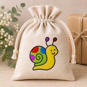 May include: A beige fabric drawstring pouch featuring an embroidered snail with a yellow body and a green spiral shell decorated with red, blue, and purple polka dots. The bag has a gathered top with two cream-colored rope drawstrings.