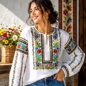 Peut inclure: Un chemisier blanc à manches longues orné de motifs floraux brodés multicolores complexes le long de la patte de boutonnage avant et des manches. Le vêtement présente une encolure fendue et est associé à un jean bleu en denim.