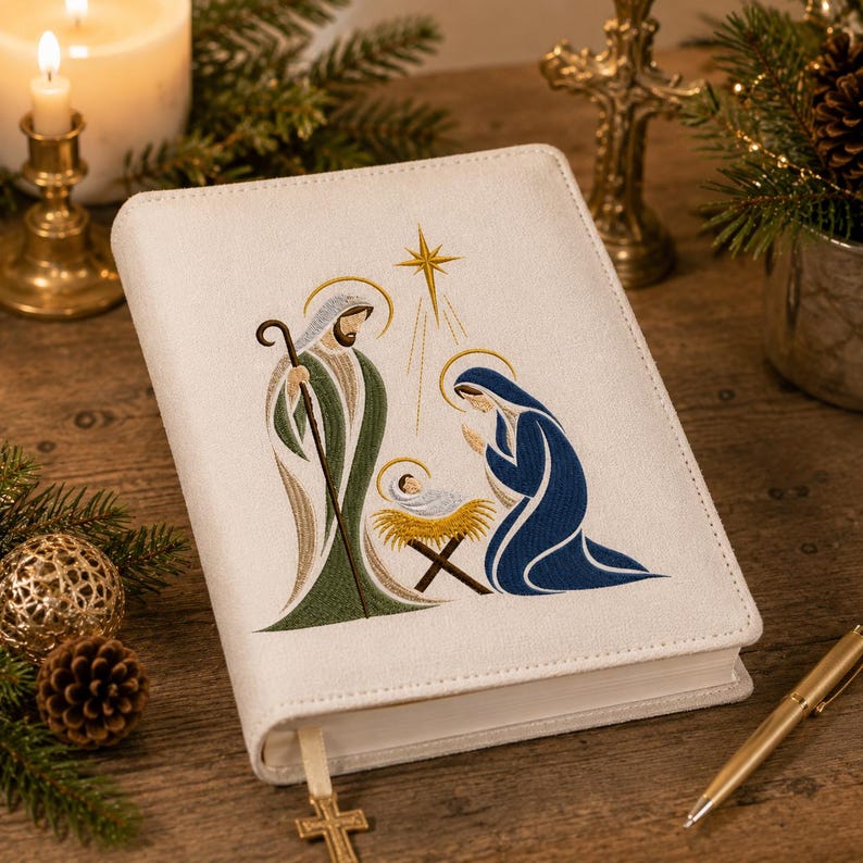 May include: A white hardcover book featuring an embroidered nativity scene on the front cover. The design depicts a figure in green robes holding a staff, a figure in blue robes kneeling, and a baby in a manger beneath a gold star.