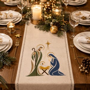 May include: A beige fabric table runner featuring an embroidered nativity scene with a central star, Joseph in green and gold robes, Mary in a blue robe, and a baby in a manger, set on a wooden dining table with white plates and glassware.