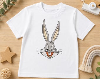 Può includere: Una t-shirt bianca a maniche corte con un ricamo a macchina centrato raffigurante il muso di un coniglio grigio con orecchie lunghe, baffi neri e un ampio sorriso che mostra due denti frontali. Il design è nei toni del grigio, bianco e beige.