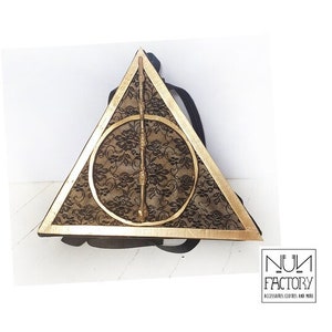 May include: A black backpack with a gold triangle design featuring a circle with a wand inside. The triangle is outlined in gold and the circle is filled with black lace.