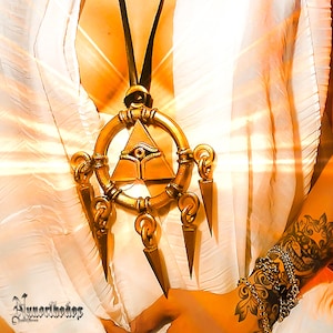 Pode incluir: Um colar dourado com um grande pingente que apresenta um olho dentro de um triângulo. O pingente é cercado por um círculo com cinco pontas que se estendem a partir dele. O colar é usado por uma pessoa com uma tatuagem no braço.