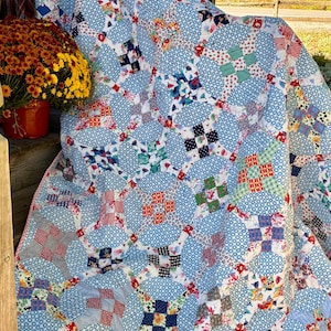 May include: A patchwork quilt featuring a repeating pattern of light blue circular shapes with white dots. The quilt is constructed from various fabric squares in red, green, blue, and white, displaying floral, plaid, and checkered prints.