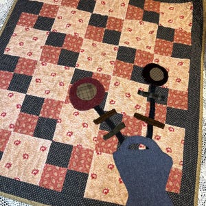 May include: A patchwork quilt with a black and white checkered pattern and a floral design. The quilt features a blue bucket, brown sticks, and red and brown circles.