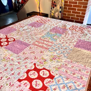 May include: A patchwork quilt with a floral pattern in shades of pink, red, and blue. The quilt features various geometric shapes and patterns, including squares, rectangles, and circles. The quilt is made of soft fabric and has a quilted texture.