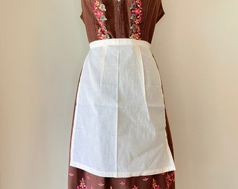 May include: A brown dirndl dress with a white apron. The bodice features floral embroidery in pink and yellow, with a zipper closure. The skirt has a matching floral embroidered hemline. The dress is displayed on a mannequin.