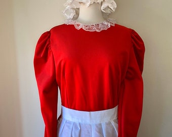 May include: A red dress with long sleeves and a white apron. The dress has a white lace collar and a matching white bonnet. The outfit is displayed on a mannequin, suggesting a costume or themed attire.
