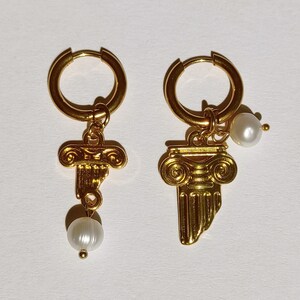 May include: A pair of gold hoop earrings with a gold charm of a column and a white pearl dangling from each earring.