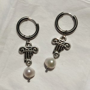 May include: A pair of silver hoop earrings with a pearl charm and a silver charm shaped like a column with scrolls.
