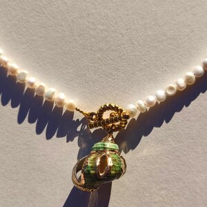 Op de afbeelding: Een witte parelketting met een gouden sluiting en een groene en gouden schelp hanger.