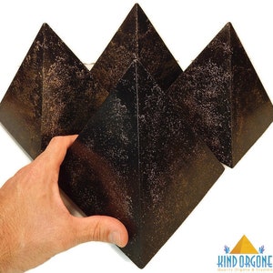 May include: Three dark brown, pyramid-shaped objects with a textured, speckled surface finish. The pyramids have a smooth, geometric form with four triangular sides meeting at a sharp apex. A logo in the corner reads Kind Orgone Quality Orgone & Crystals.