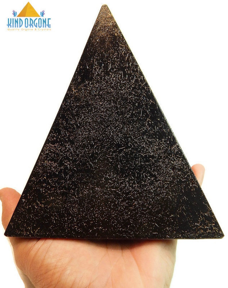 May include: A black pyramid-shaped object with a textured surface featuring fine, light-colored metallic-like flecks throughout. The top left corner displays the text KIND ORGONE with a small yellow pyramid icon and blue crystal graphics.