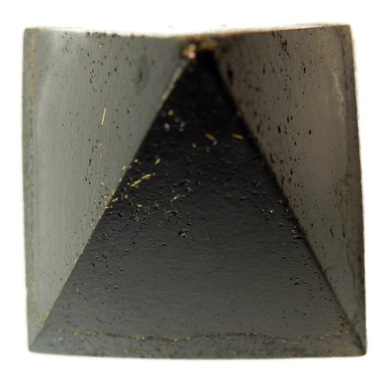 May include: A solid black pyramid-shaped object with a textured, porous surface. The four triangular faces meet at a central apex, and the base is square. The material appears dark and matte with small indentations and flecks across the surface.