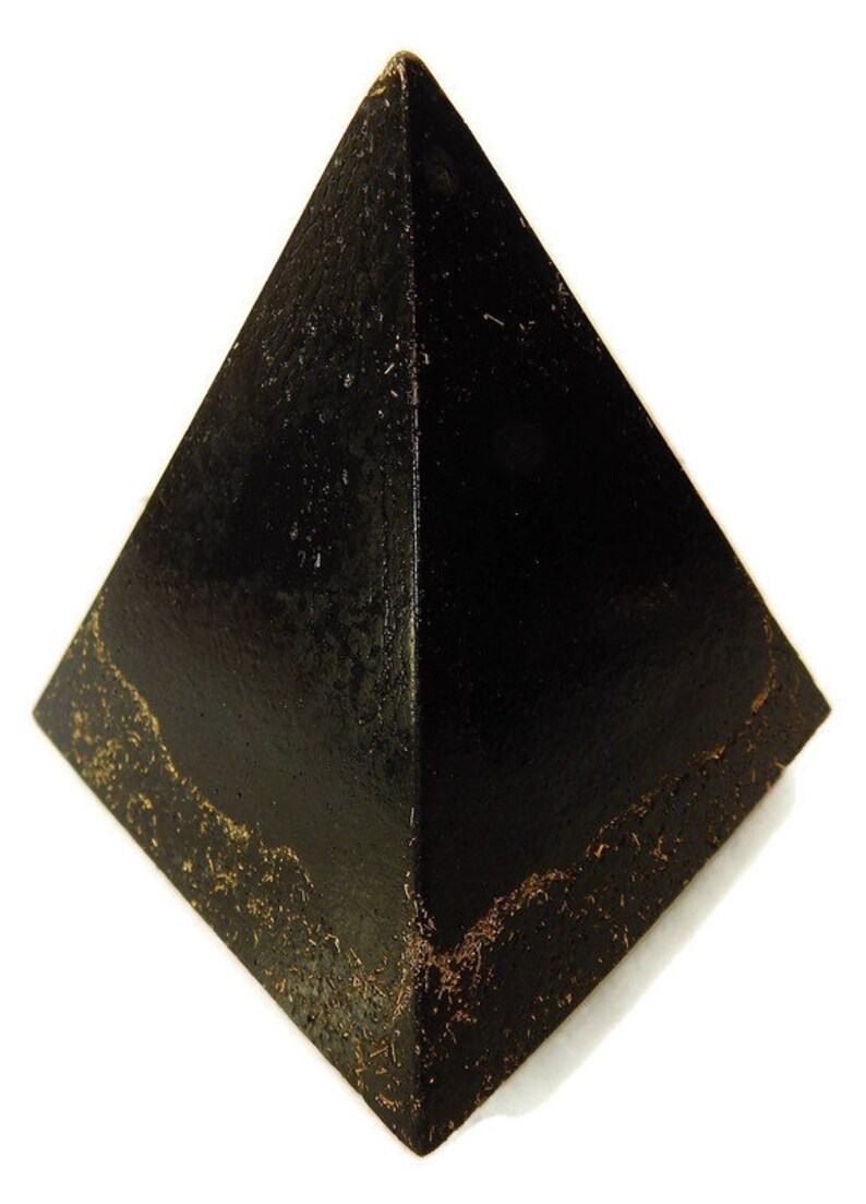 May include: A black pyramid-shaped object with a smooth, dark surface and a textured, weathered base. The four triangular faces meet at a sharp apex, and the bottom edges show a rough, granular, and brownish-gold distressed finish.