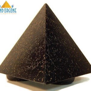 May include: A black pyramid-shaped object with a textured surface featuring fine, light-colored, hair-like inclusions throughout. The top left corner displays a logo with a yellow pyramid icon and the text KIND ORGONE Quality Orgone & Crystals.