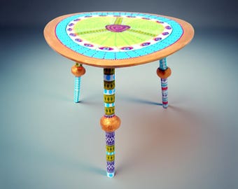 Könnte beinhalten: Ein dreibeiniger Beistelltisch mit dreieckiger Tischplatte, die ein hellgrünes Zentrum, eine violette Spirale und einen blauen Rand mit kleinen Punkten aufweist. Die drei Beine sind mit bunten geometrischen Mustern und goldenen Kugeln verziert.